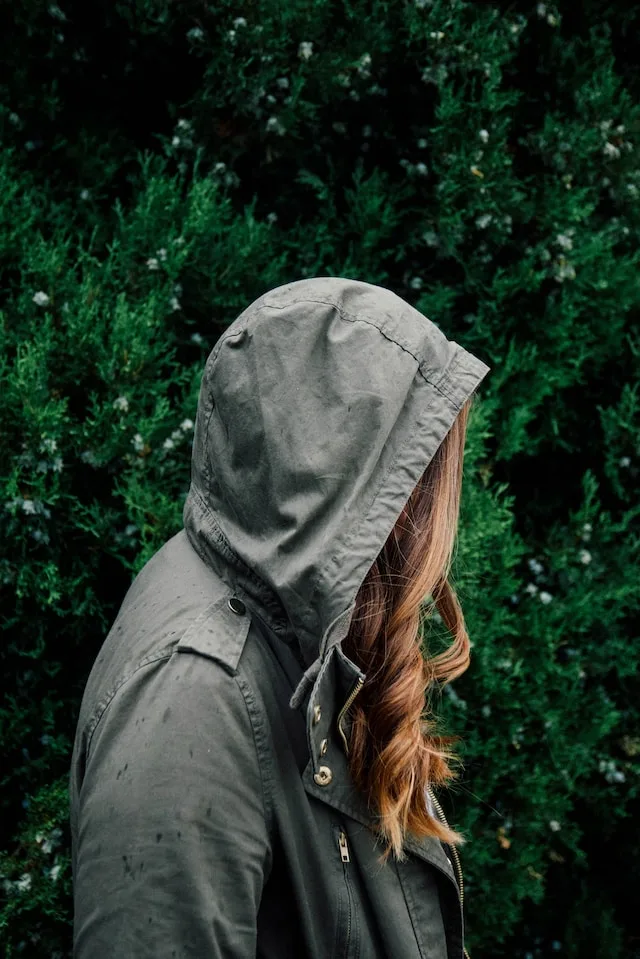 Sad woman walking with fear, not showing her face, dark green hoodie up with red hair curls flowing out