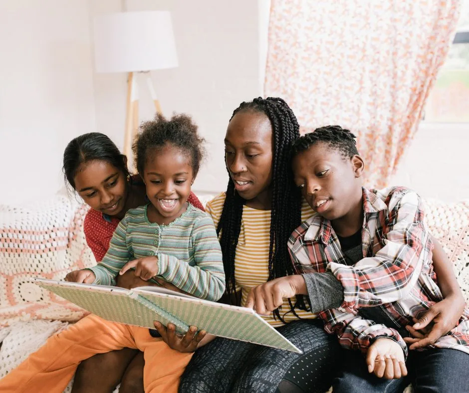 a family of 4 reading a book with the youngest child seating on the mother's lap