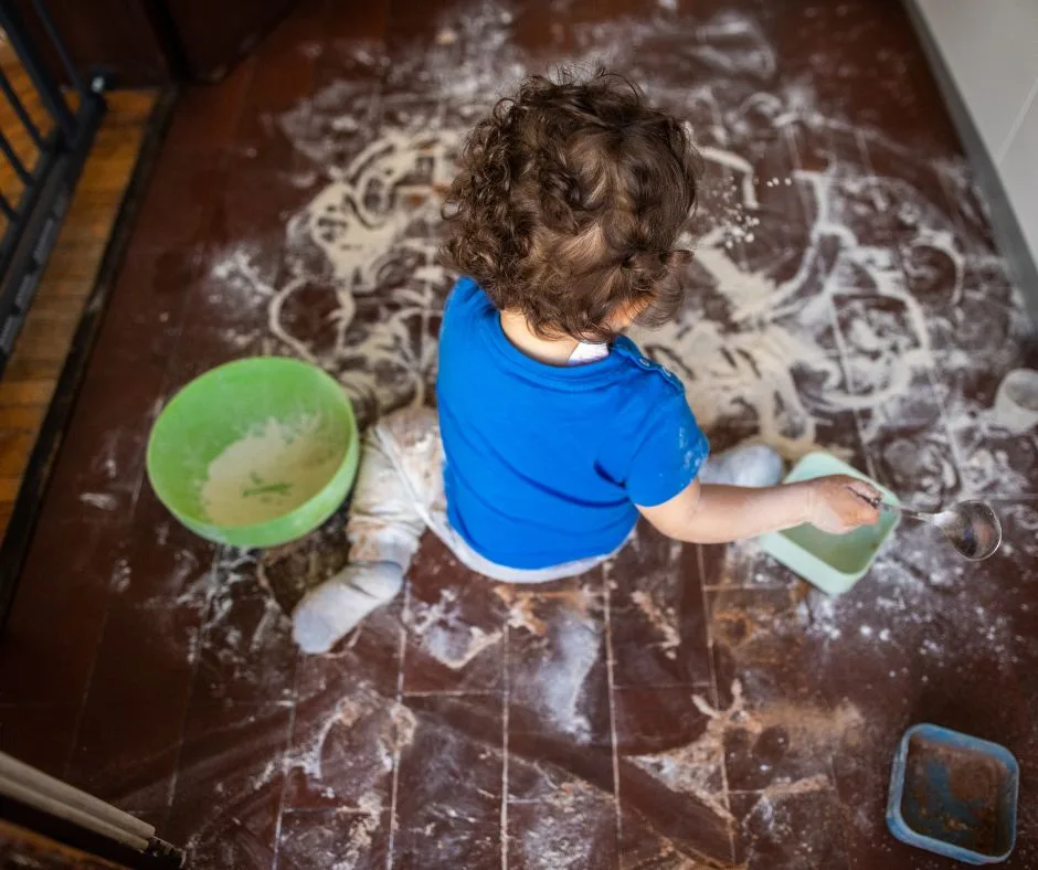 a todller playing with flour spread all over the floor