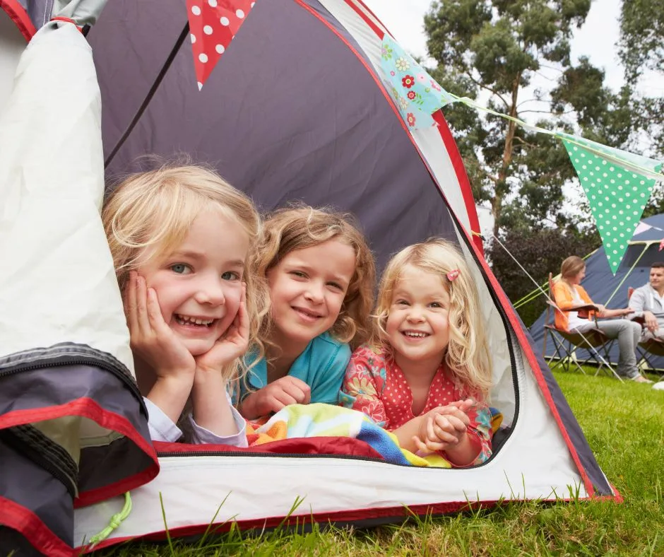 3 girls smiling poking their heads outside the tent
