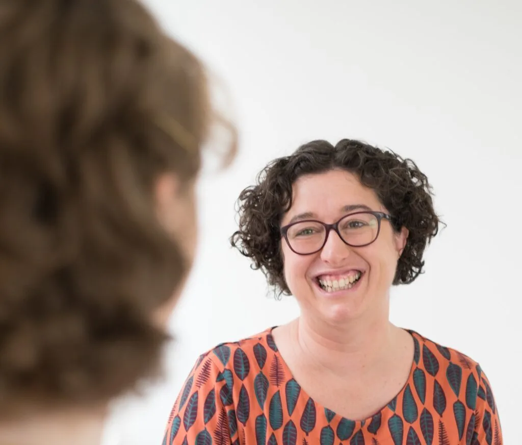 Woman in orange dress is coaching a client while smiling.