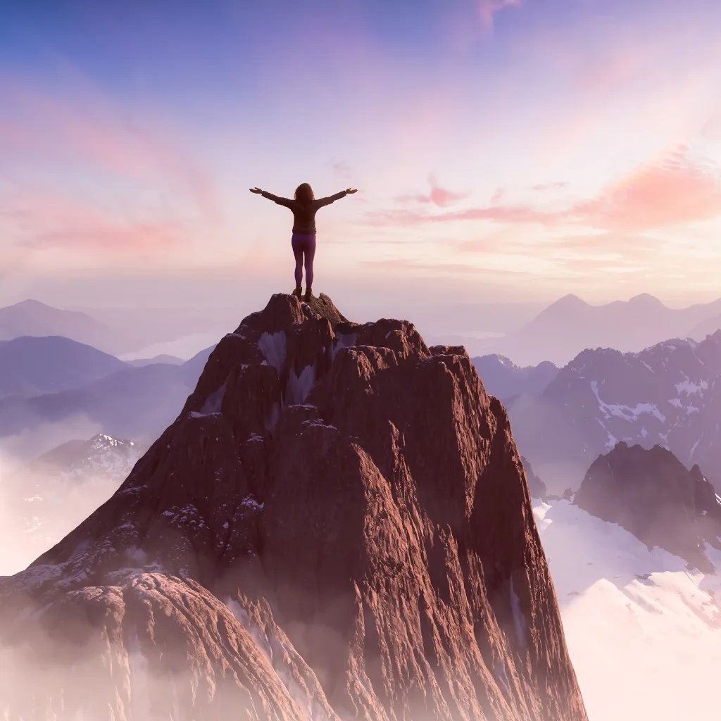 Woman standing on top of a mountain, looking out to the pink and purple sun rise. Photo representing empowerment and achievement for Survive to Thrive Group Coaching.